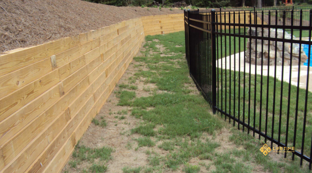 Timber retaining wall built with horizontal wooden beams, supported by gravel base, creating a rustic landscape border.