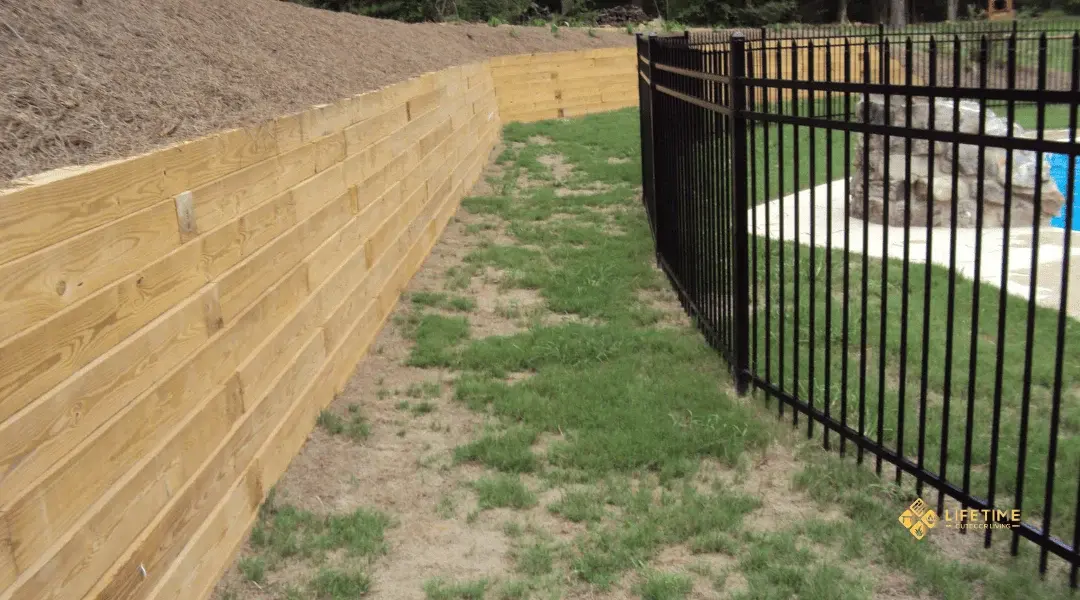 Timber retaining wall built with horizontal wooden beams, supported by gravel base, creating a rustic landscape border.
